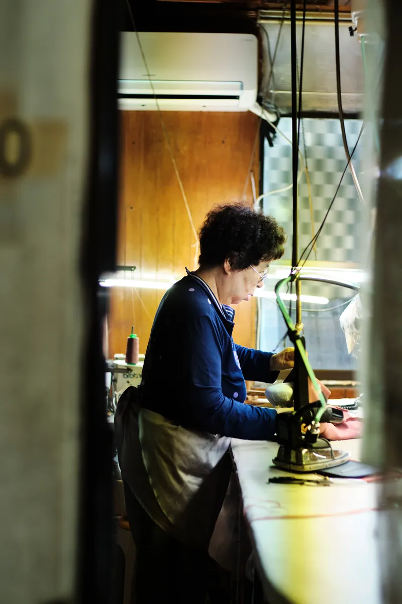 Woman in a blue cardigan sewing at a machine, seen through a narrow gap
