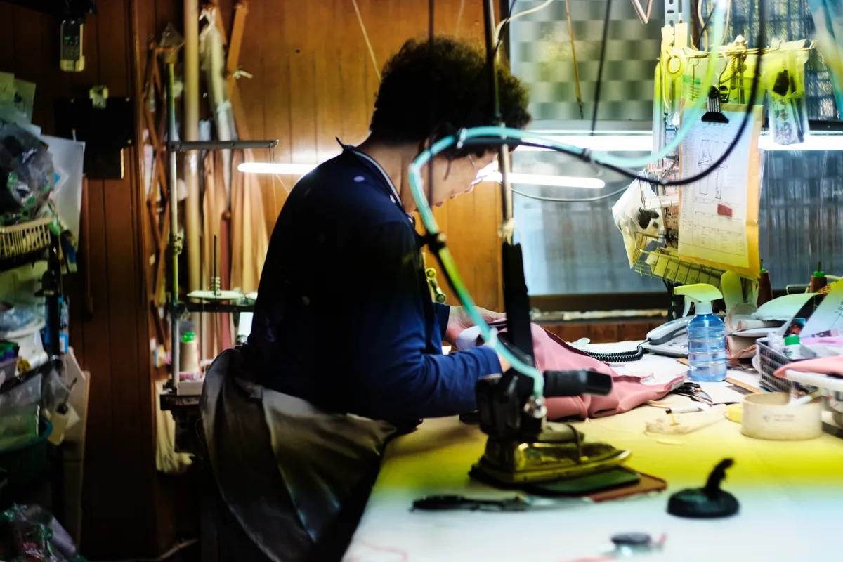 Woman in a blue cardigan sewing at a machine in a tailor shop
