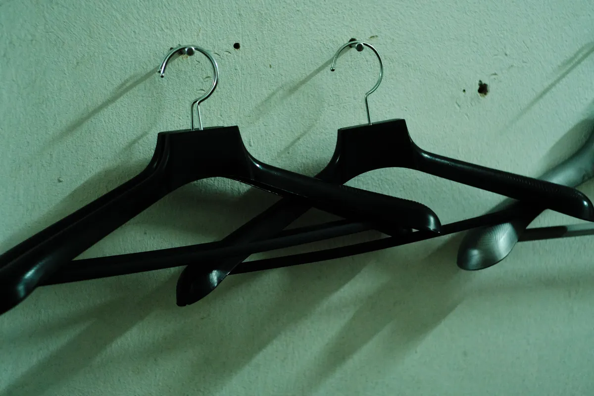 Two black coat hangers on a pale green wall