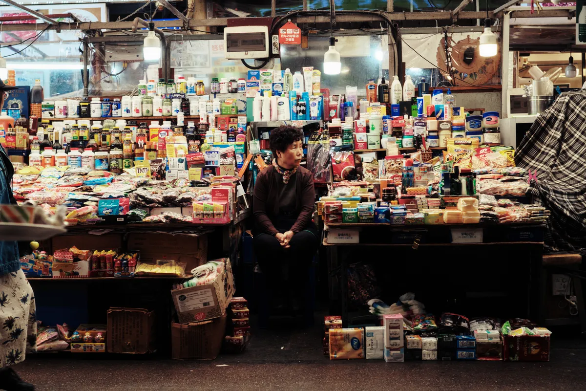 Vendor sitting among colorful goods at a market stall