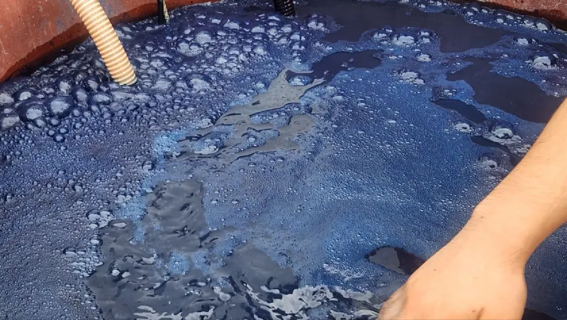 Dark indigo vat with coppery-blue foam at the edge