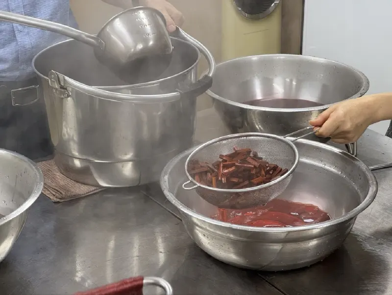 Straining boiled sappanwood chips into a steel basin