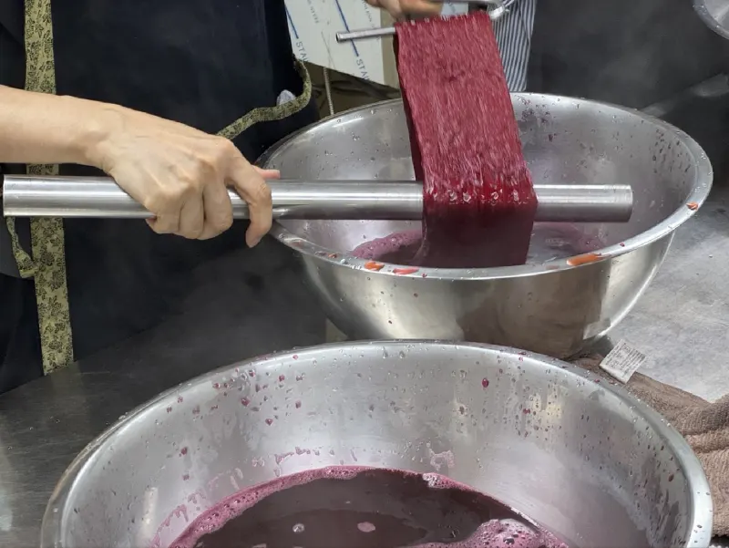 Skein dyed crimson on a steel rod over a basin of dye