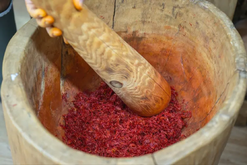 Pounding dried safflower petals in a wooden mortar