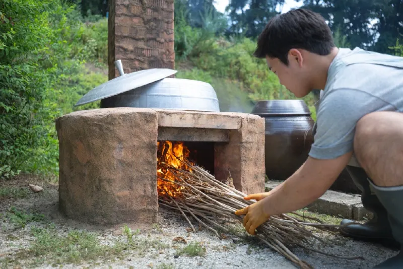 Feeding dried stalks into the fire under the cauldron