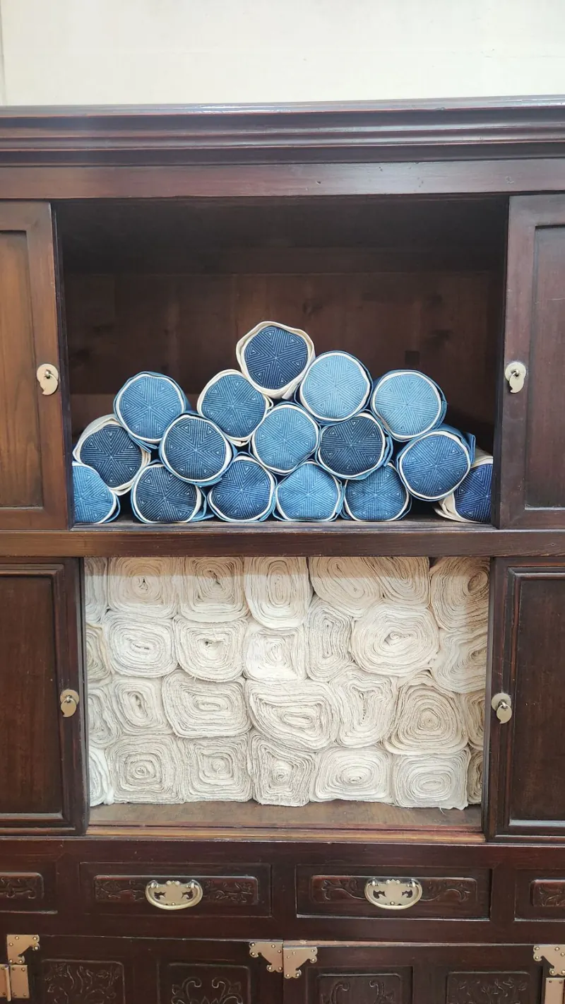 A wooden cabinet holding rolls of indigo-dyed cloth
